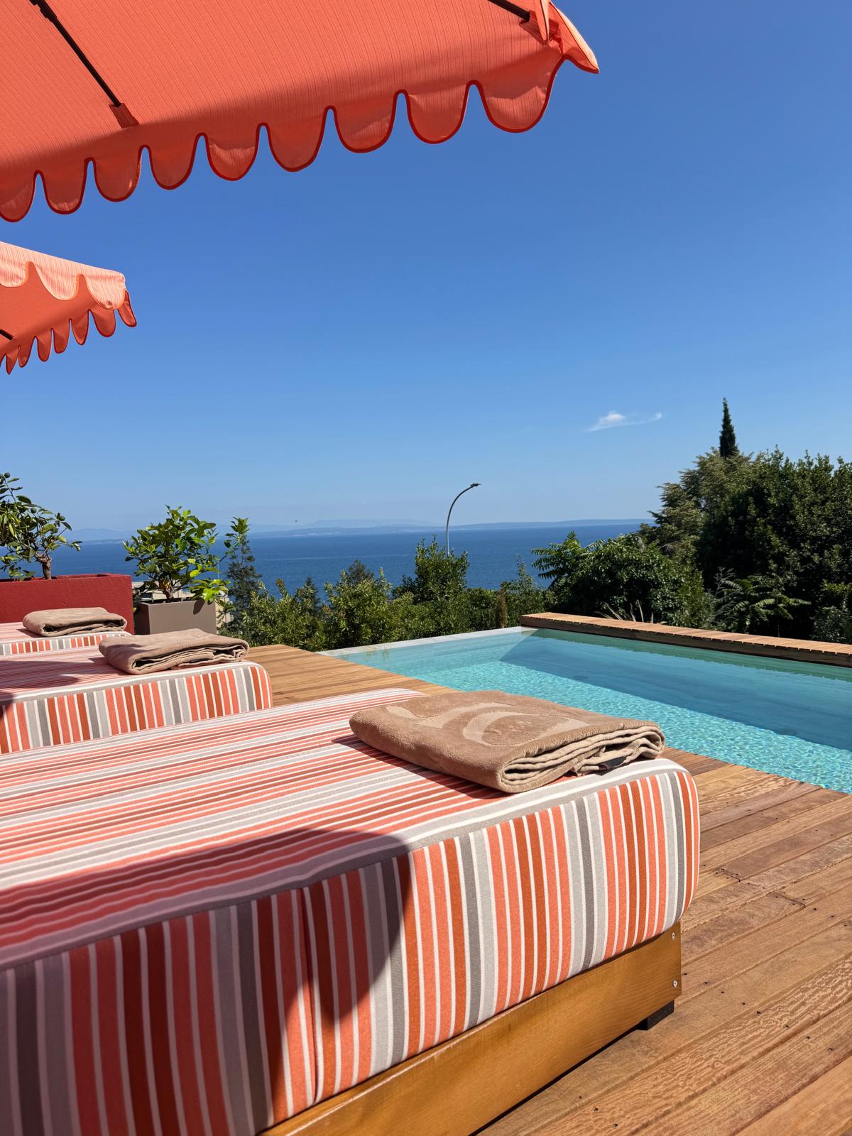 Sun loungers on the teak pool deck beside the infinity pool with Kvarner Bay sea view