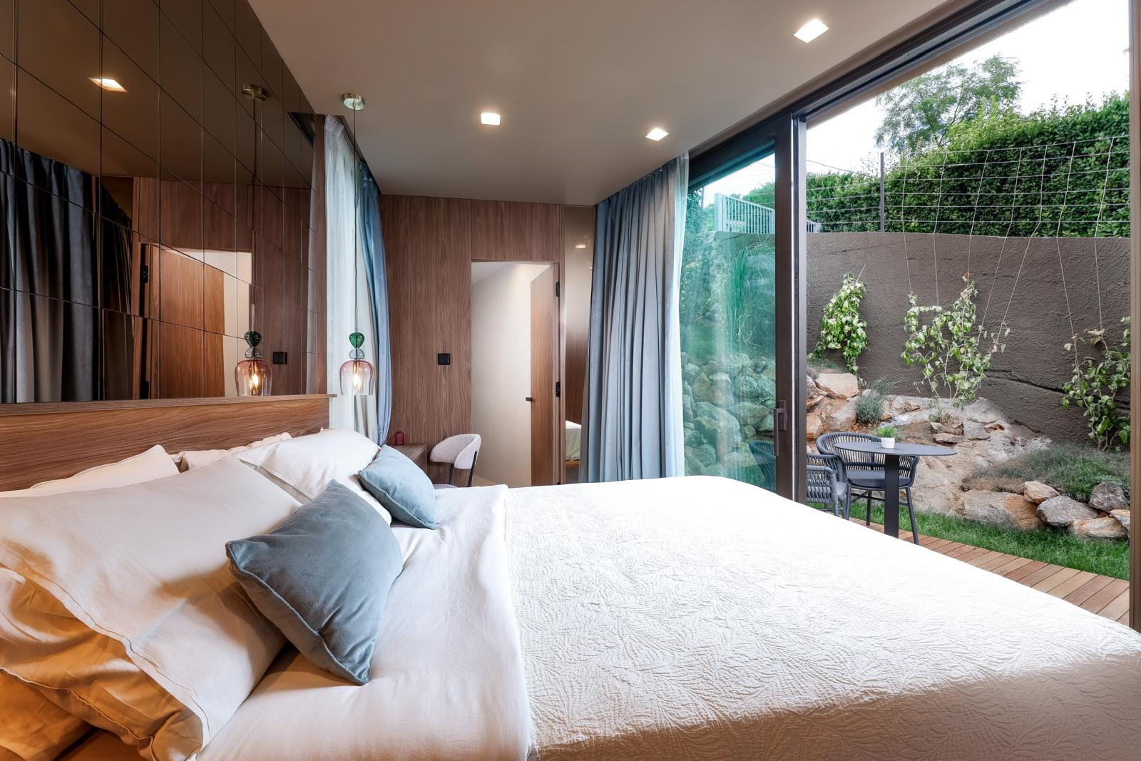 Bedroom with floor-to-ceiling glass opening onto a private decked garden terrace