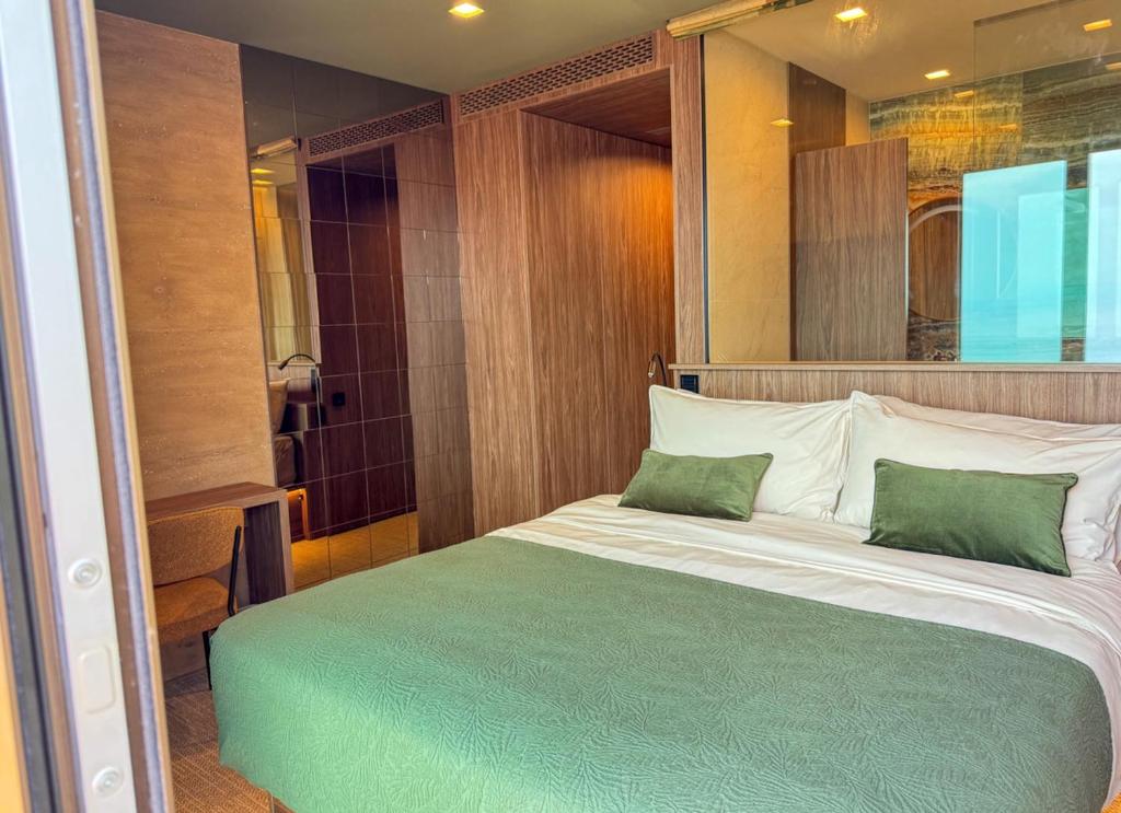 Bedroom with emerald green bedding, walnut panelling and glass-walled en-suite bathroom